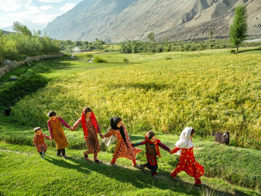 Afghan children holding hands as they walk beside a wheat field in a mountain valley